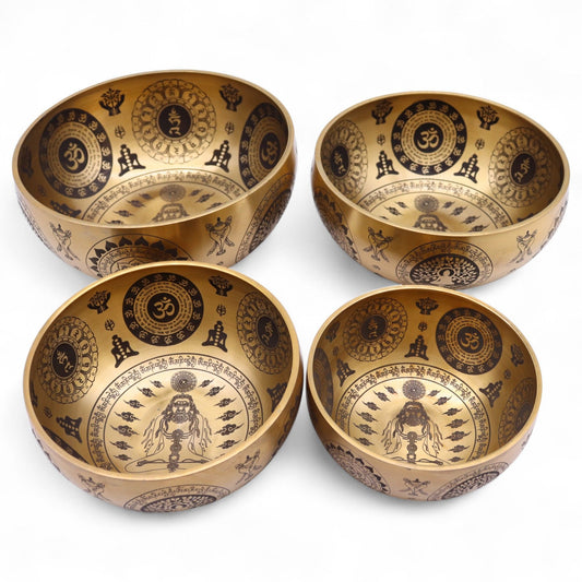 Set of four handcrafted brass singing bowls with intricate yogic etchings and spiritual symbols on a dark background.