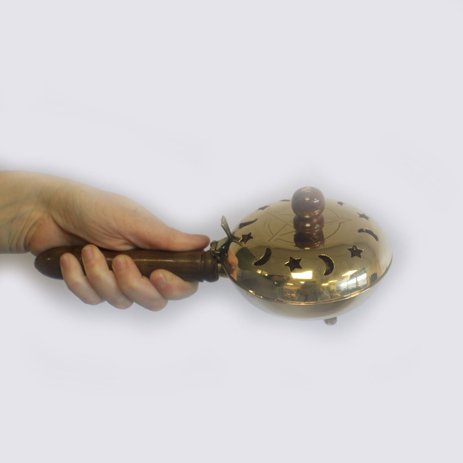Polished brass incense burner with a pentagram lid, wooden handle, and star and moon cut-outs for aromatic smoke release.