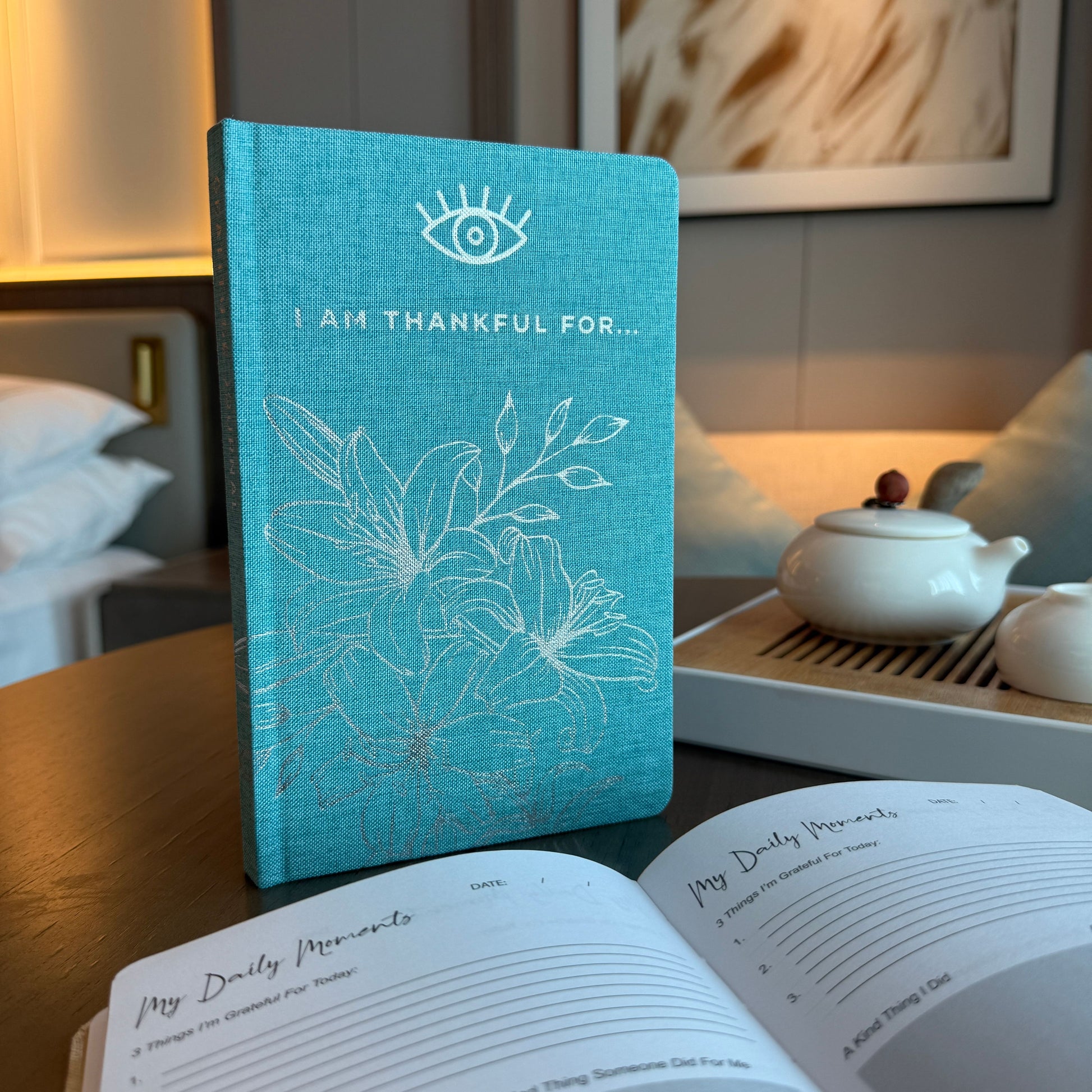 Blue textured hard cover gratitude journal with silver floral detailing and an elegant eye symbol.
