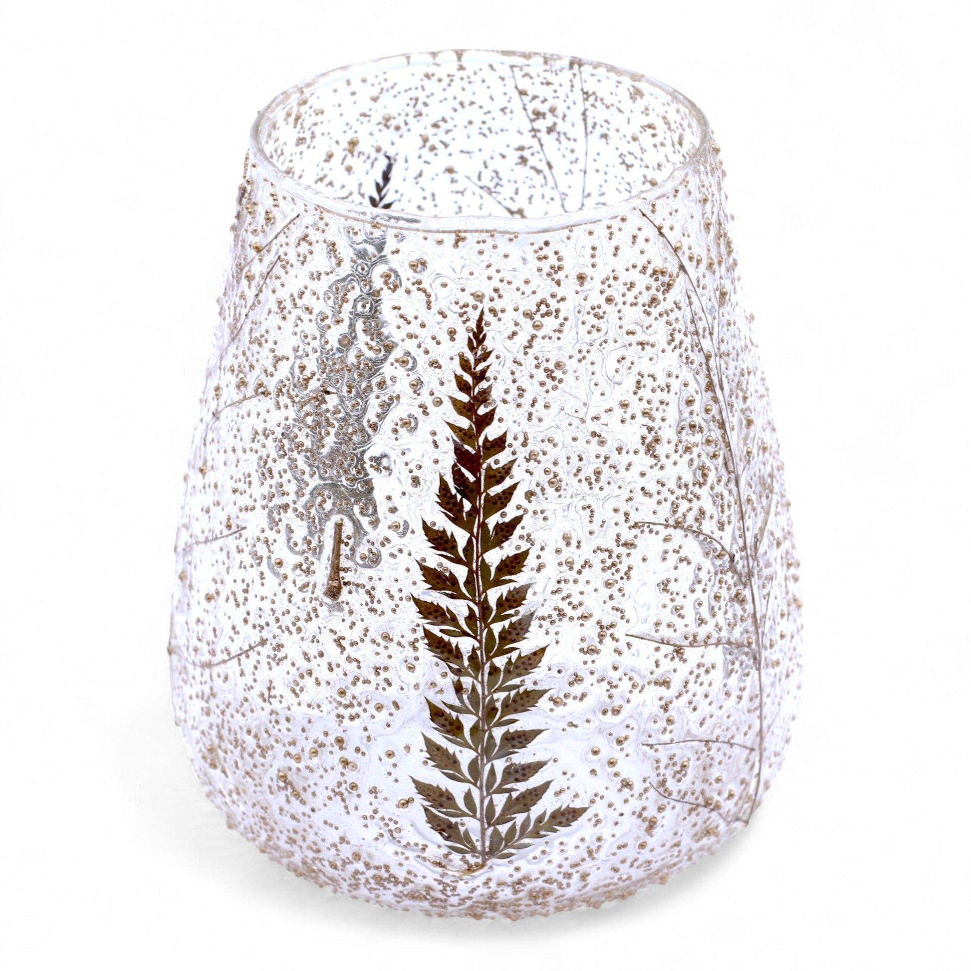 Large bowl-shaped glass candle holder with real embedded fern leaves and delicate branches on a textured surface.