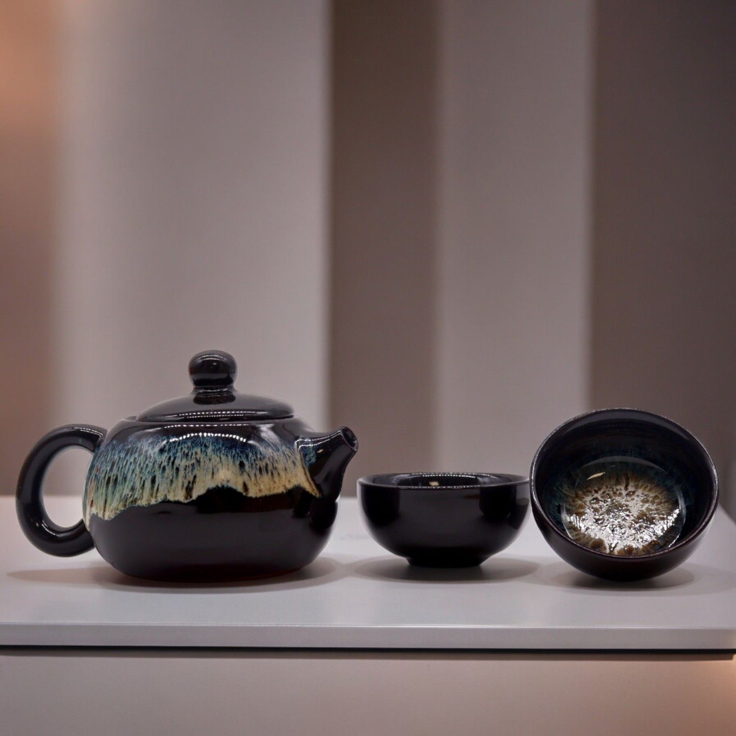 Sophisticated matte black glaze teapot with two matching small cups on a minimalist background.