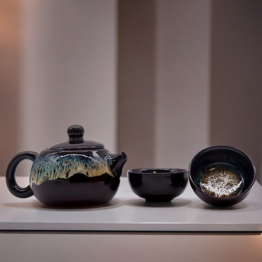 Sophisticated matte black glaze teapot with two matching small cups on a minimalist background.