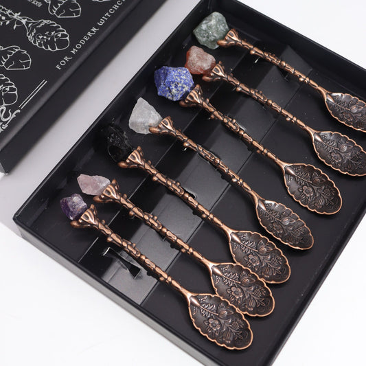 Set of seven ornate bronze spoons with various polished gemstone crystals attached to the handles.