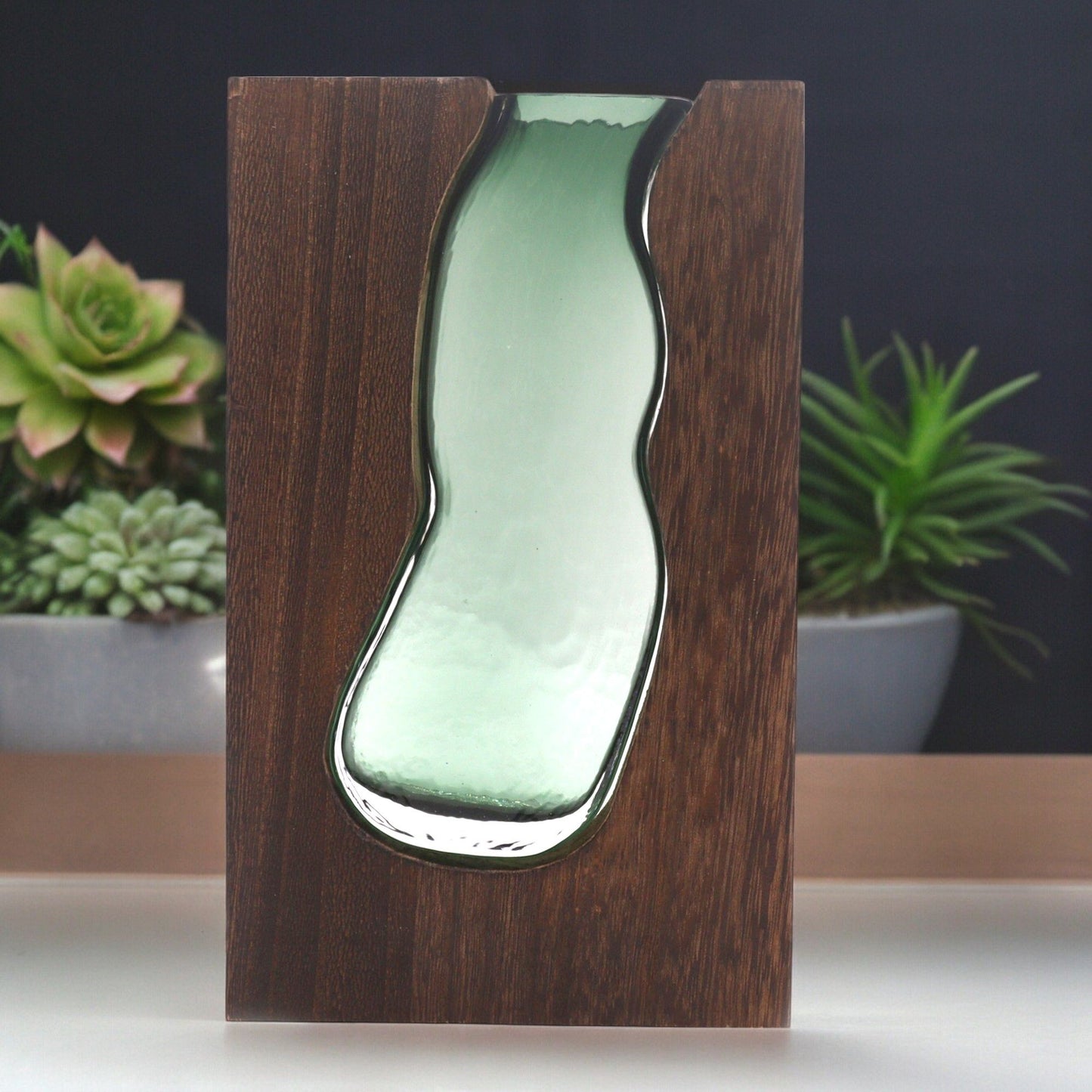 Clear glass vase sitting within a rectangular dark tung wood frame base.