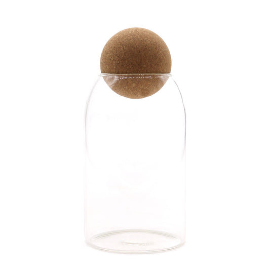 Clear cylindrical glass jar with a round spherical cork lid sitting on a neutral background.