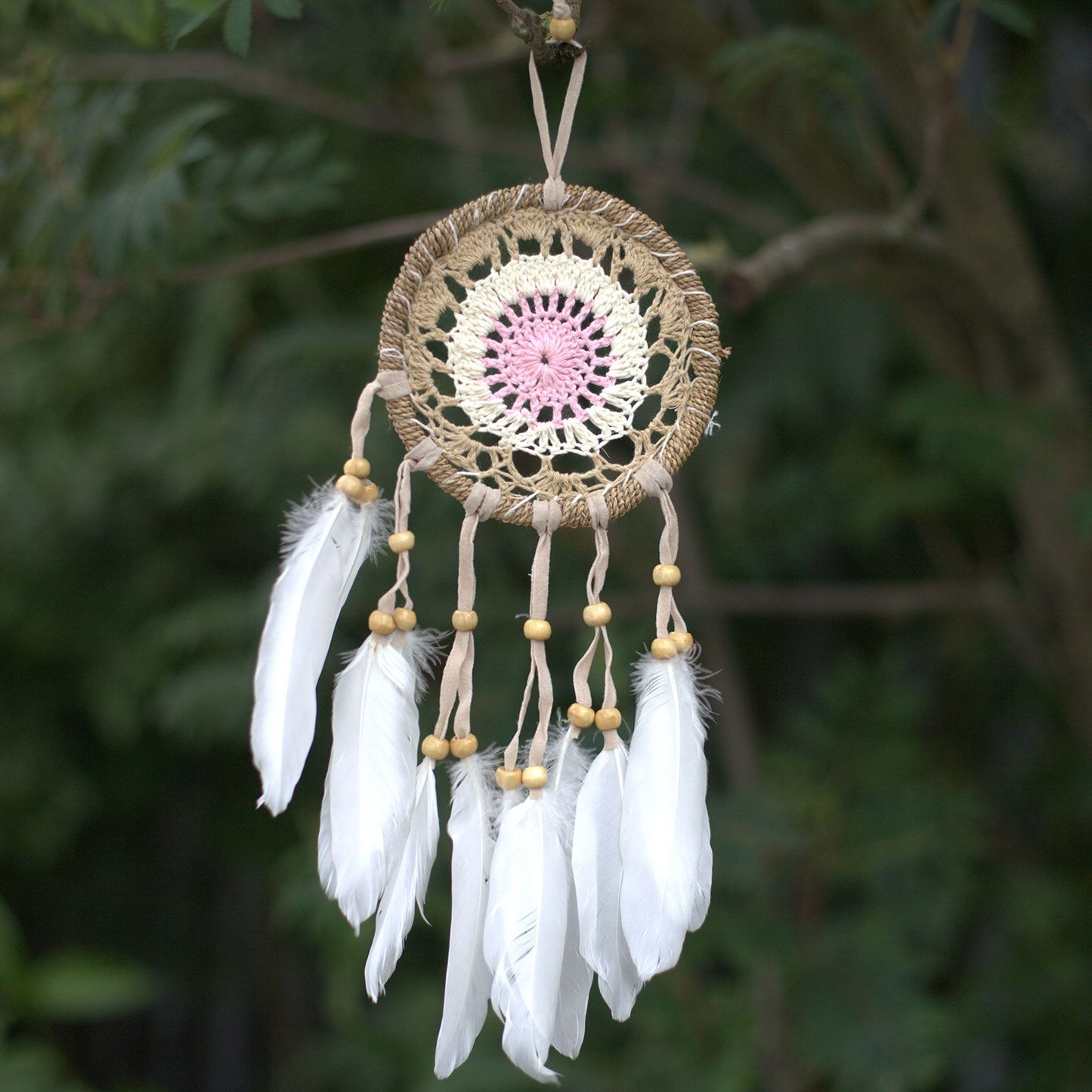 Delicate pastel pink macramé dream catcher with a woven web and hanging cotton tassels.