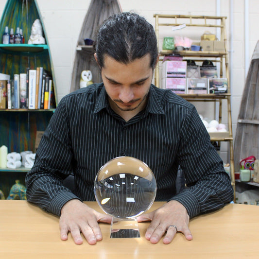 Large clear glass crystal ball resting on a minimalist wooden stand on a plain surface.