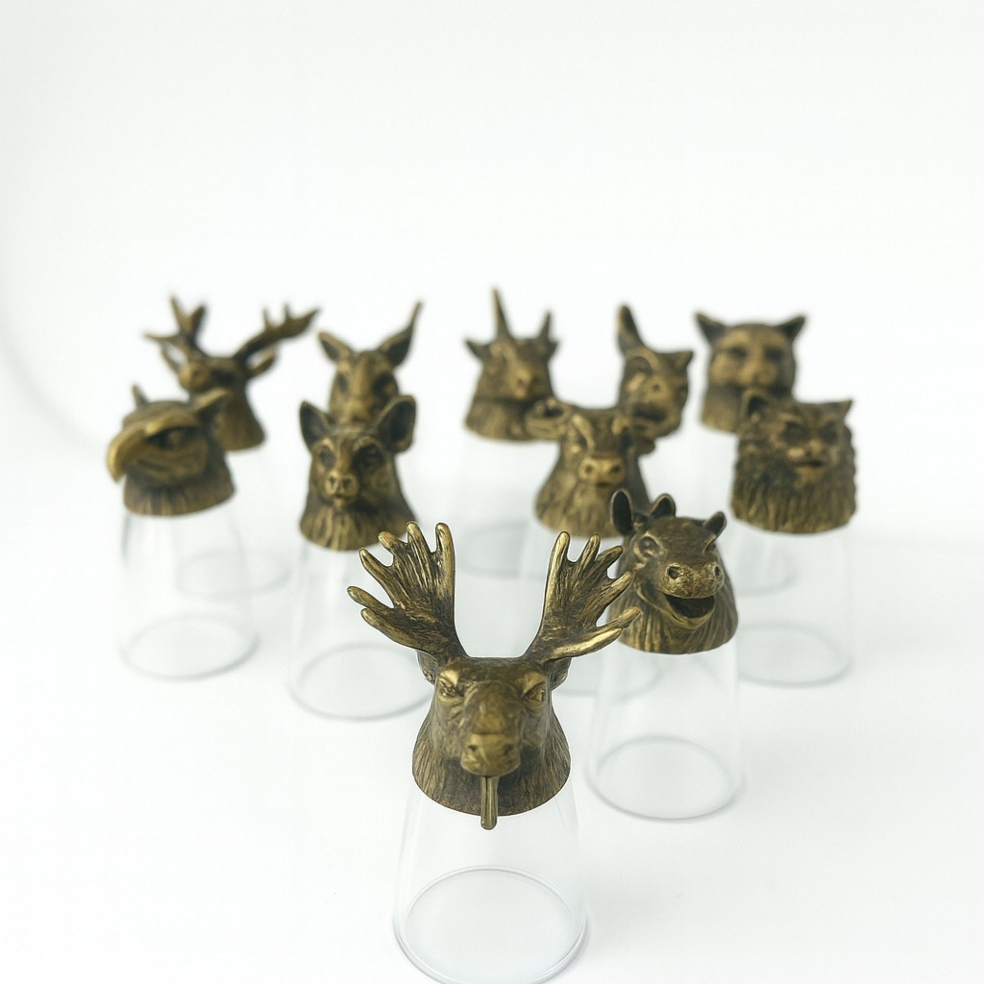 Twelve glass shot glasses with detailed antique bronze bases shaped like mystical forest animals and creatures.