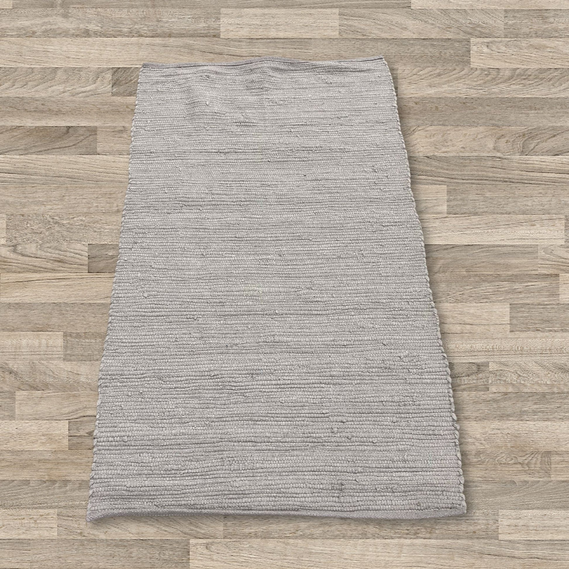 Handwoven small rectangular cotton rug in a soft grey shade with a subtle textured weave.