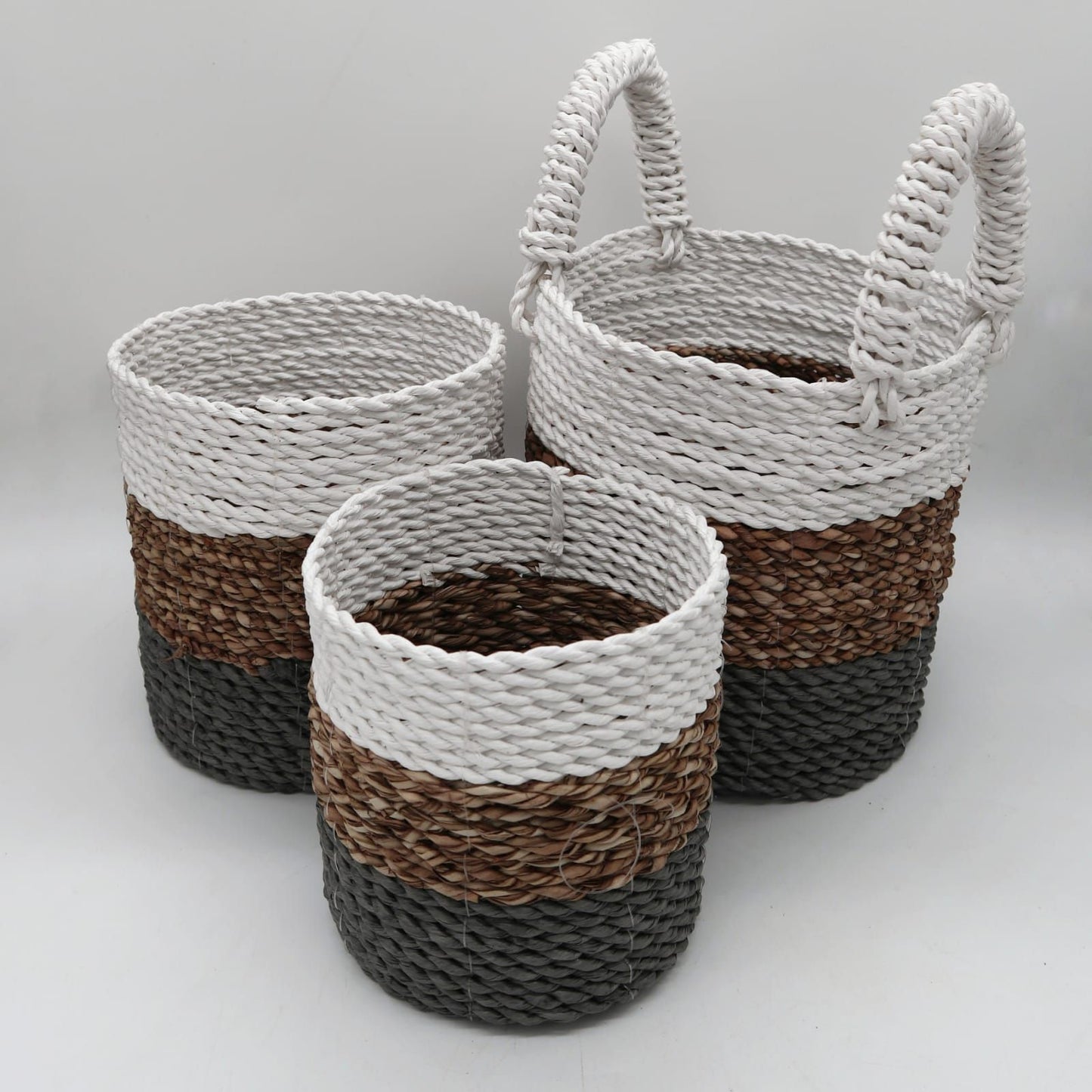 Set of three handwoven round seagrass baskets in grey, natural, and white tones, nested together.