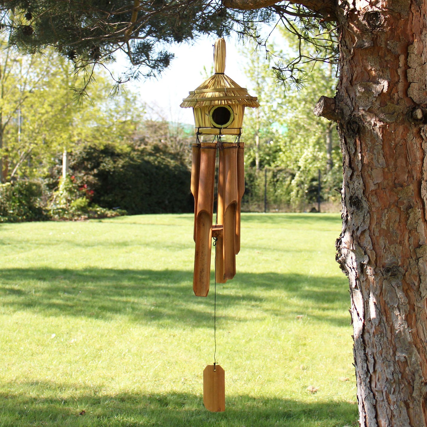 Round woven seagrass bird house with hanging metal chimes, featuring a natural rustic texture for garden decoration.