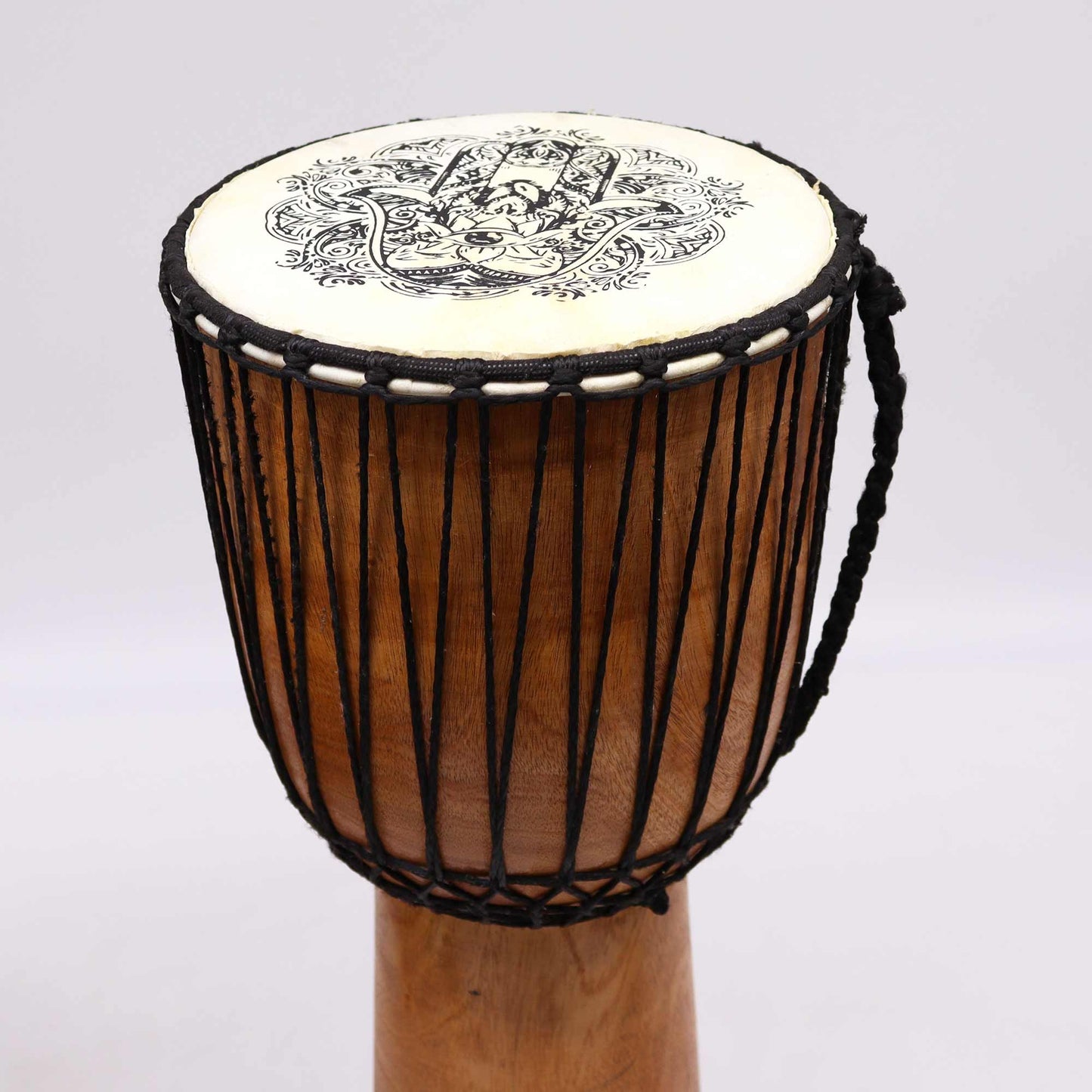 Handcrafted wooden djembe drum featuring a wide top and a decorative Hamsa symbol on the natural skin drumhead.