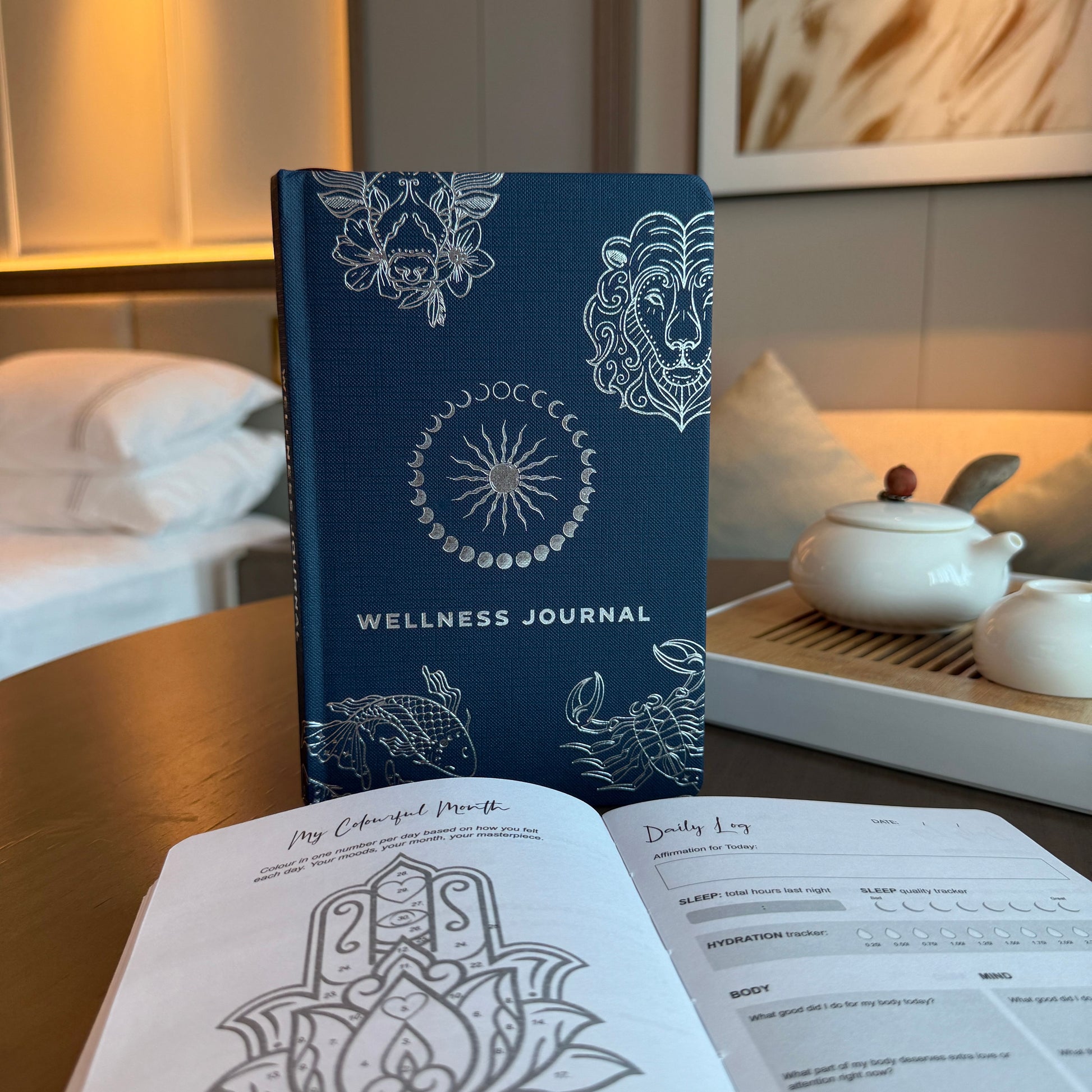 Midnight blue wellness journal with a shimmering silver zodiac and celestial star design on the front cover.