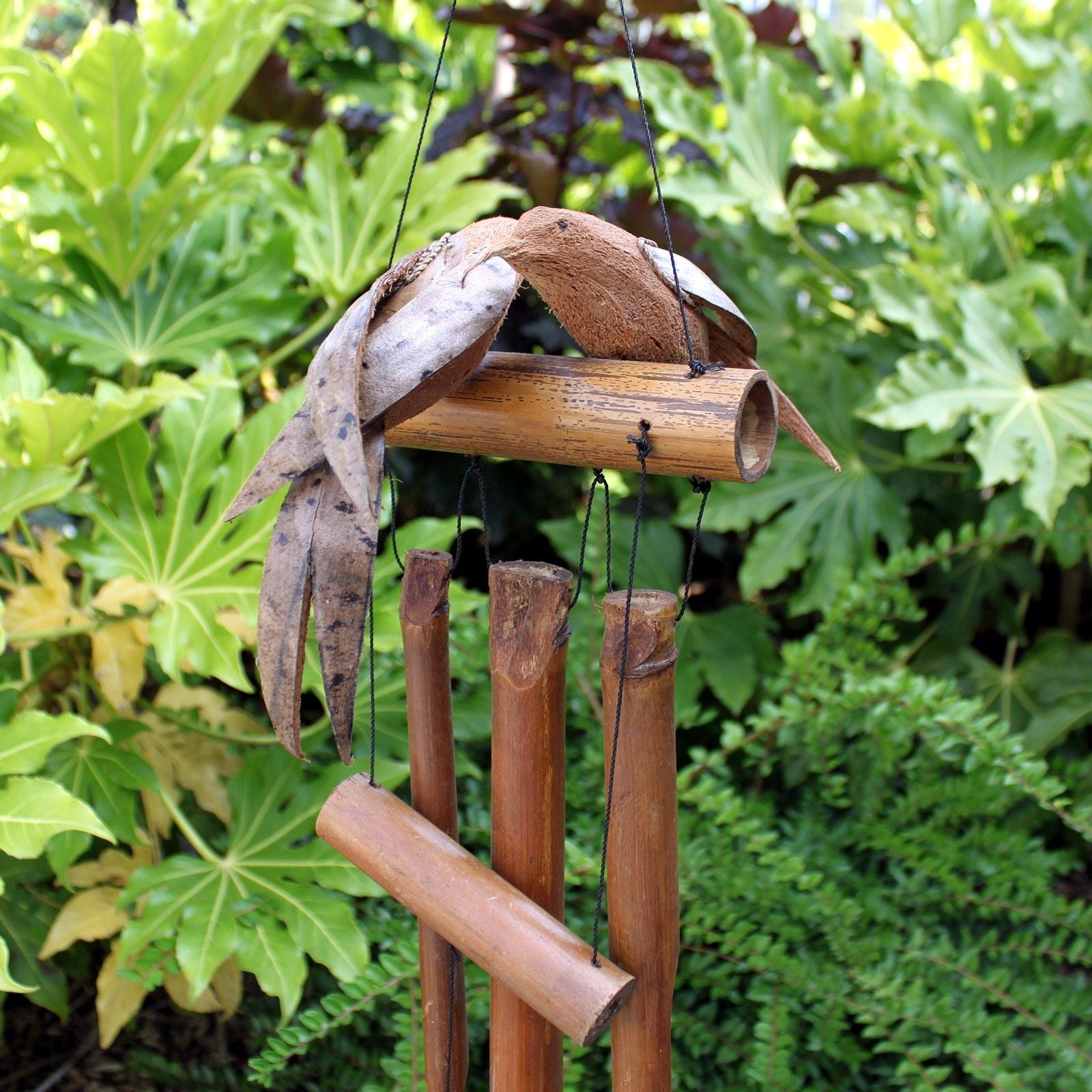 Handcrafted bamboo wind chime featuring two carved wooden birds and a coconut shell top, hanging in a natural garden setting.