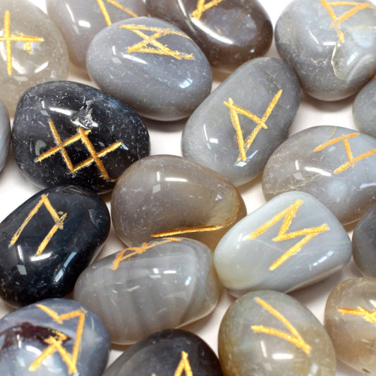 Tumbled grey agate stones engraved with mystical rune symbols, laid out next to a soft drawstring carrying pouch.