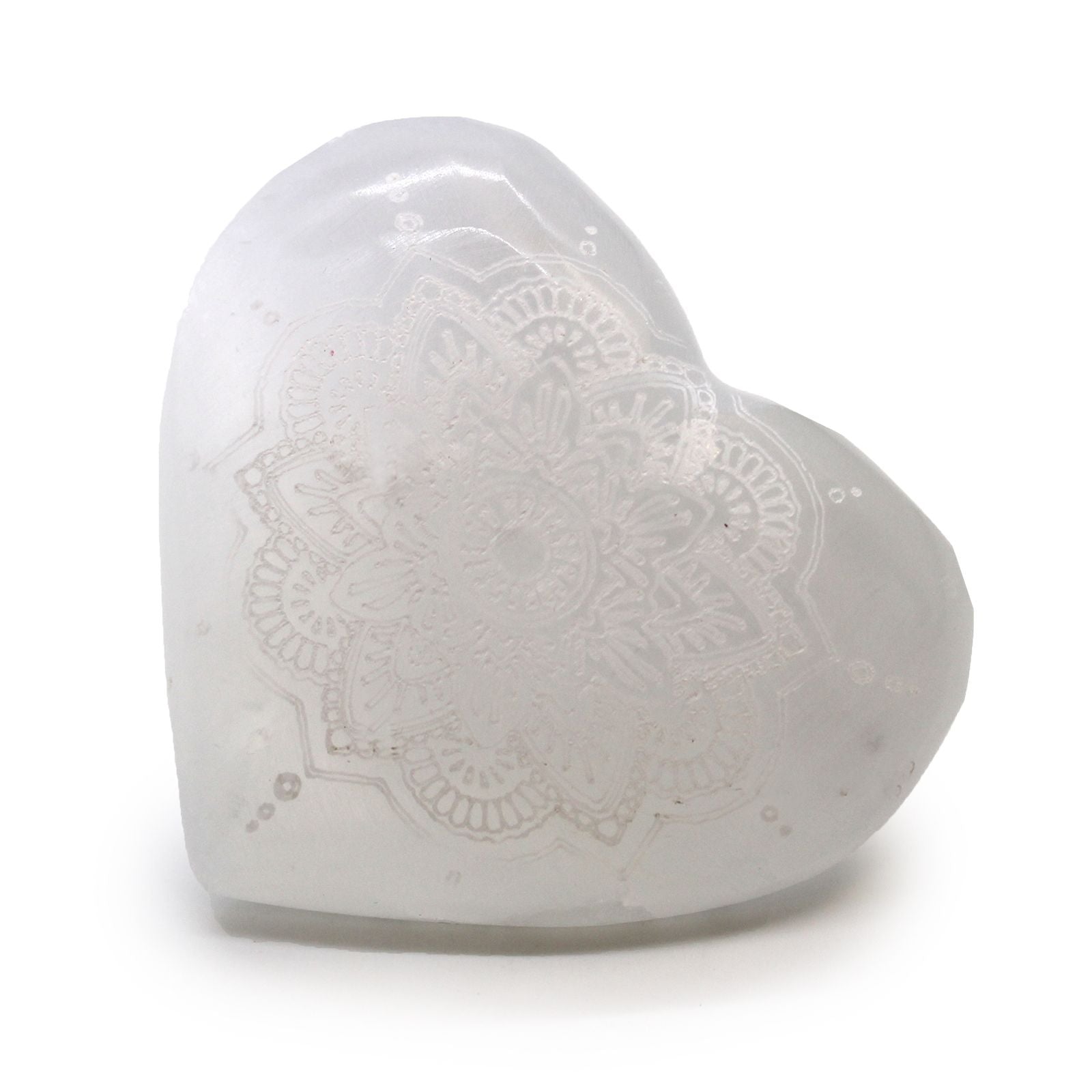 A smooth white selenite heart-shaped crystal with a detailed mandala pattern engraved on its surface.