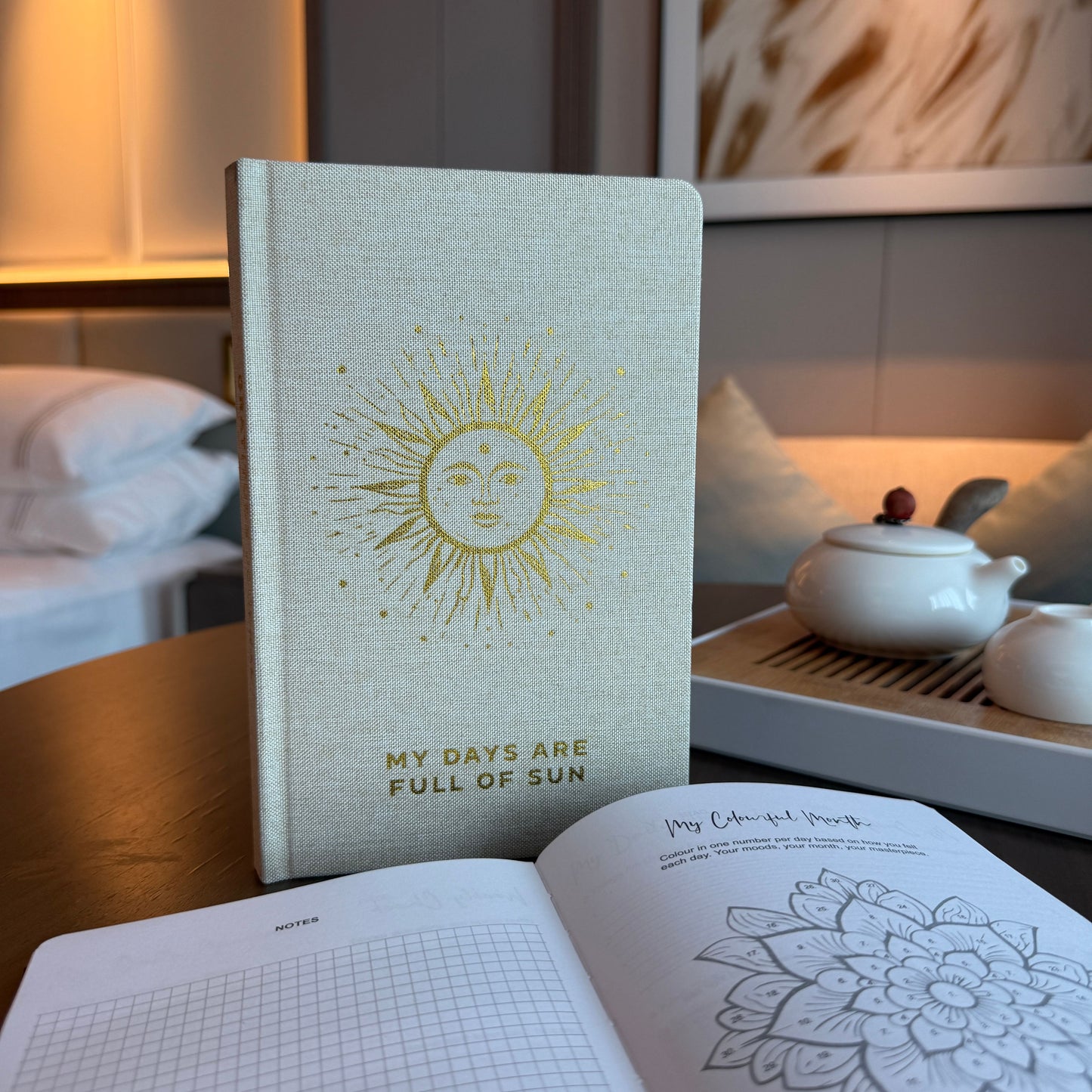 Elegant ivory gratitude journal with a golden sun design and shimmering gold page edges on a clean background.