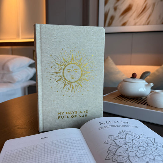 Elegant ivory gratitude journal with a golden sun design and shimmering gold page edges on a clean background.