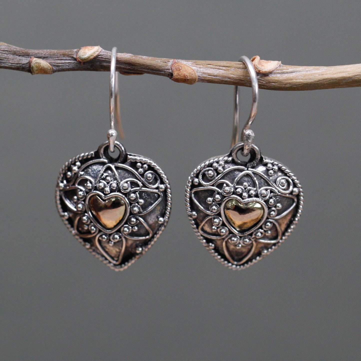 Intricate mixed metal drop earrings featuring a silver and gold mandala heart design in a decorative gift box.