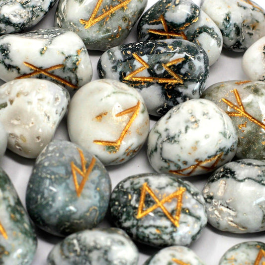 Tumbled white and green tree agate stones with engraved golden rune symbols scattered near a small drawstring pouch.