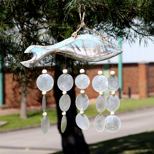 Hand-carved driftwood fish with a soft blue wash finish and translucent natural capiz shell drops on a rustic chime.
