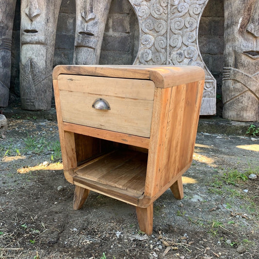 Handcrafted round bedside table made from recycled teak wood with a natural rustic finish, drawer, and open shelf.
