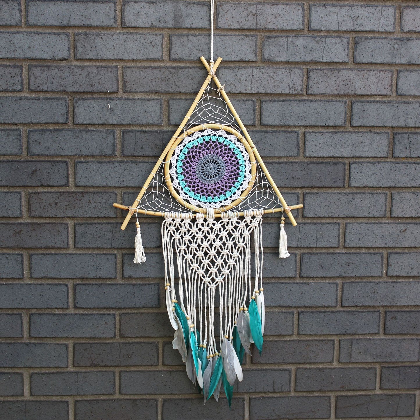Large pyramid-shaped macrame dream catcher in white and turquoise with a central protective evil eye design.