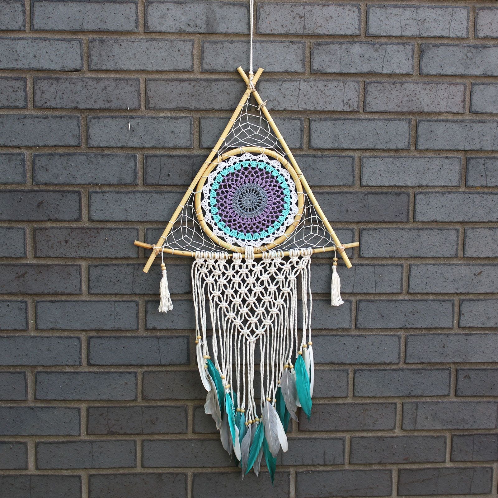 Large pyramid-shaped macrame dream catcher in white and turquoise with a central protective evil eye design.