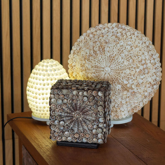 Handcrafted oval lamp made from natural white sea shells with intricate cut-out patterns for a soft glow.