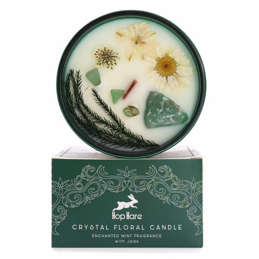 Green crystal healing candle topped with dried flowers and jade gemstones in a decorative tin with a tarot card.