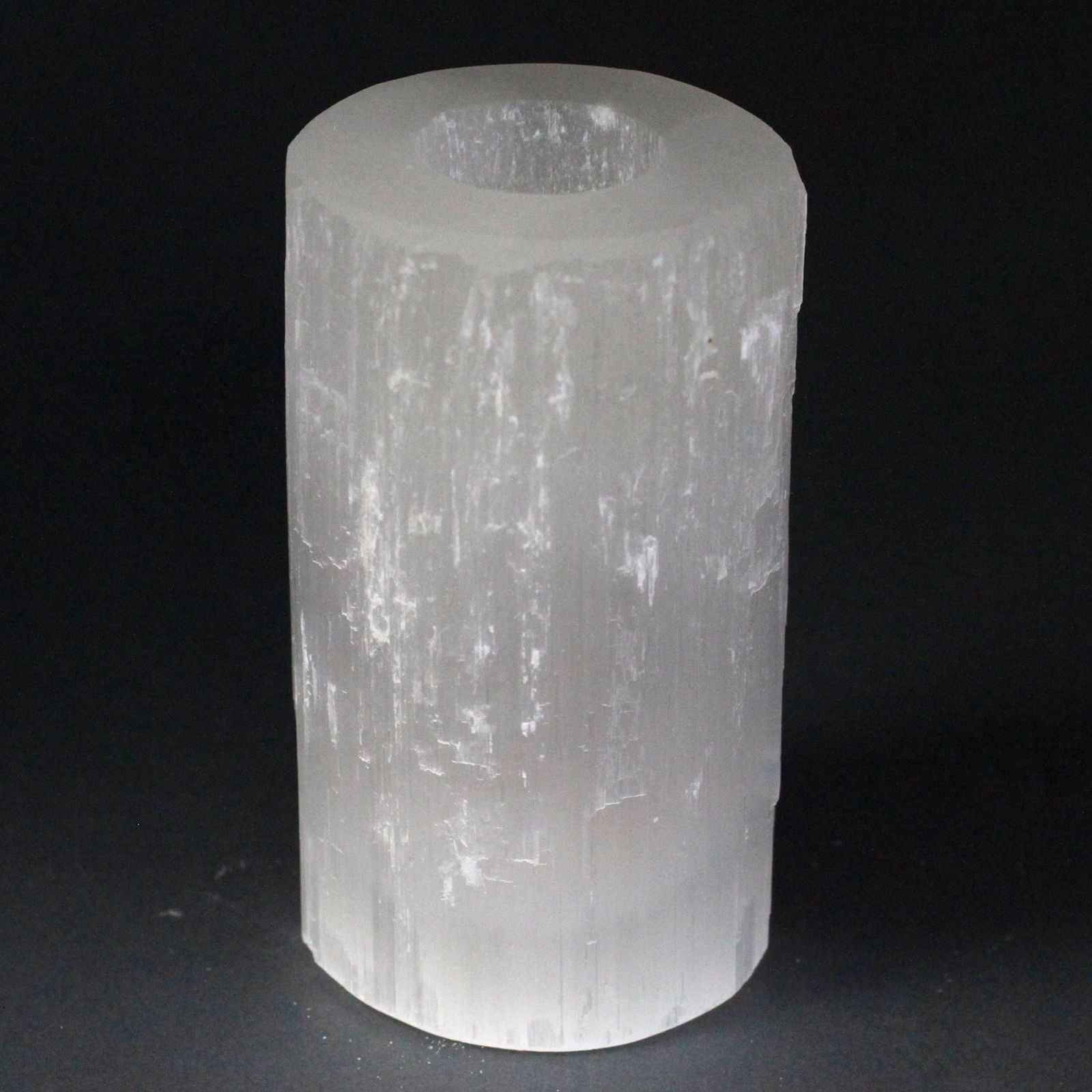 Tall white selenite crystal cylinder candle holder with natural rough edges and a translucent shimmery finish.