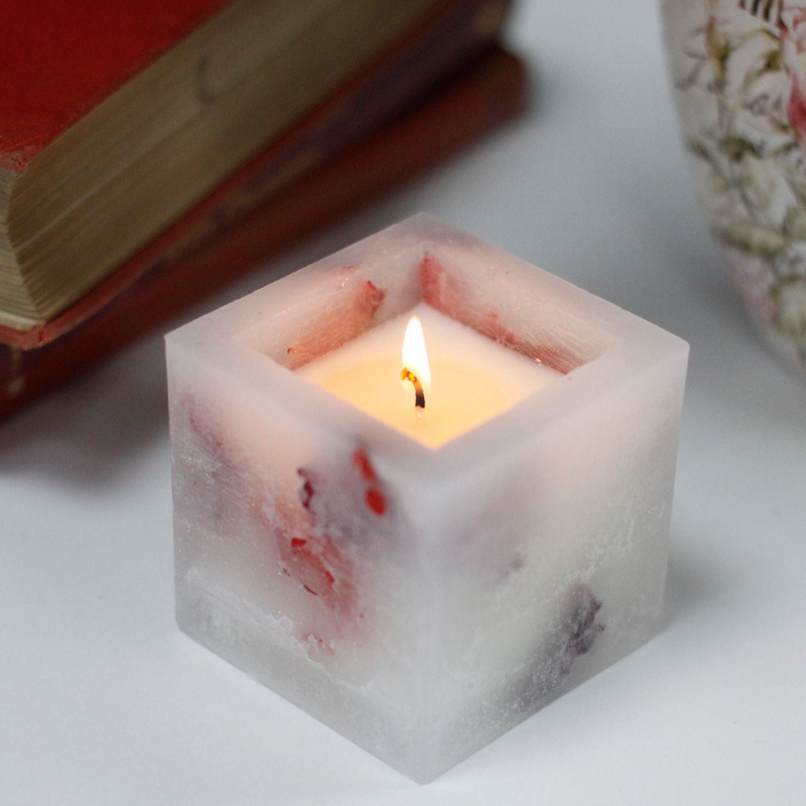 Small square glass jar candle with a rose scent and a magical glowing effect when lit.