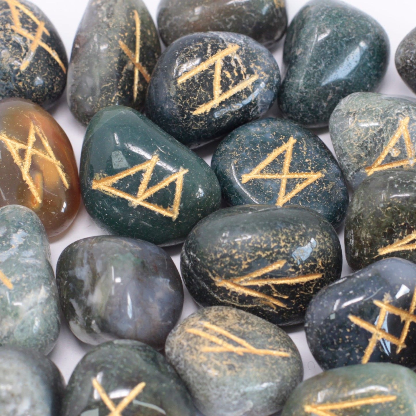 A set of smooth, green Moss Agate stones engraved with traditional rune symbols, resting in a small protective pouch.