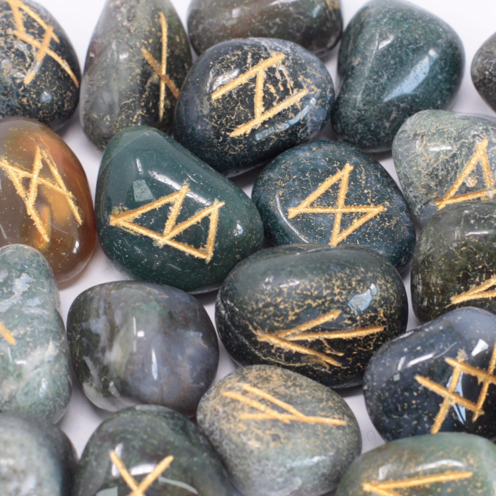 A set of smooth, green Moss Agate stones engraved with traditional rune symbols, resting in a small protective pouch.