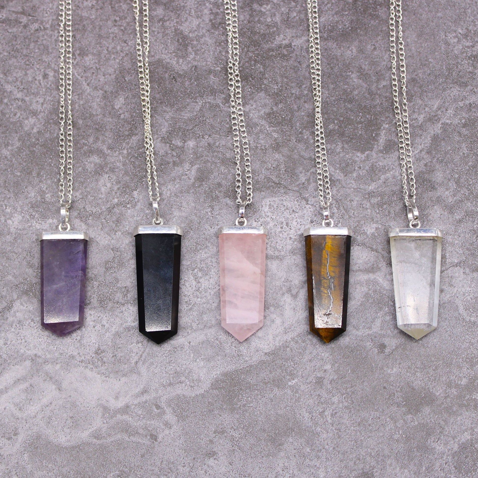 A sleek, flat pencil-shaped purple amethyst gemstone pendant with a silver-toned metal bail.