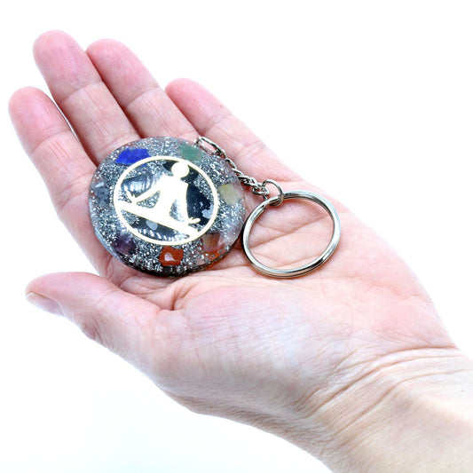 Circular orgonite keyring featuring a golden Buddha symbol over layered multi-coloured chakra gemstone chips in resin.