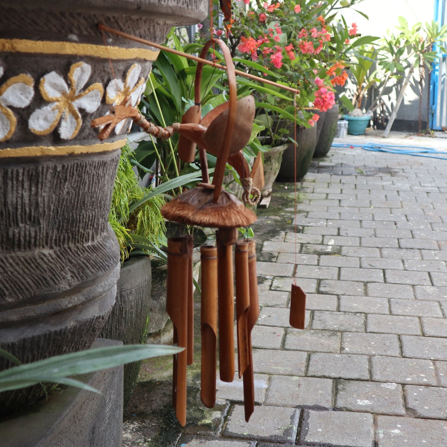 Hand-carved coconut shell dragon windchime with natural bamboo tubes hanging against a soft background.