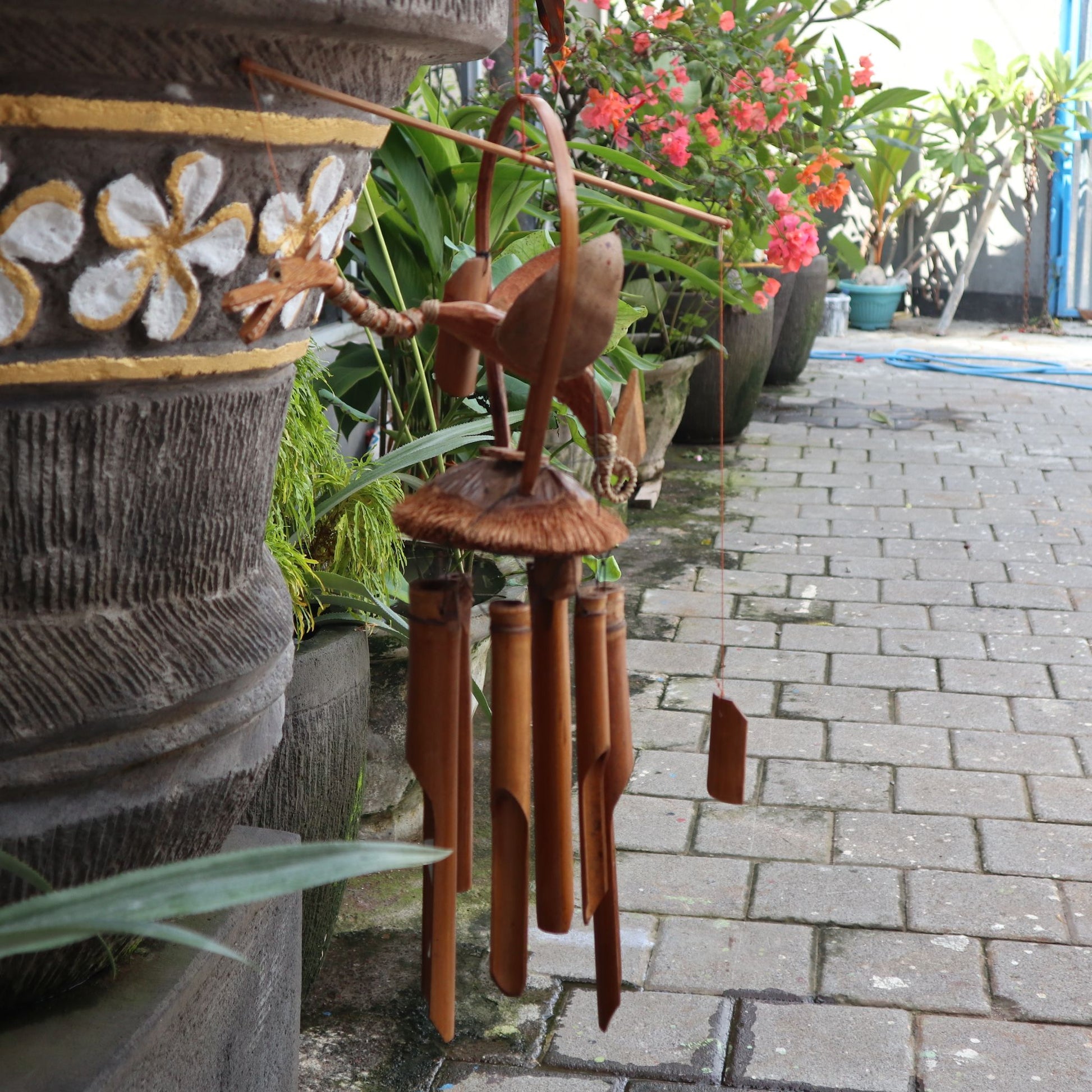 Hand-carved coconut shell dragon windchime with natural bamboo tubes hanging against a soft background.