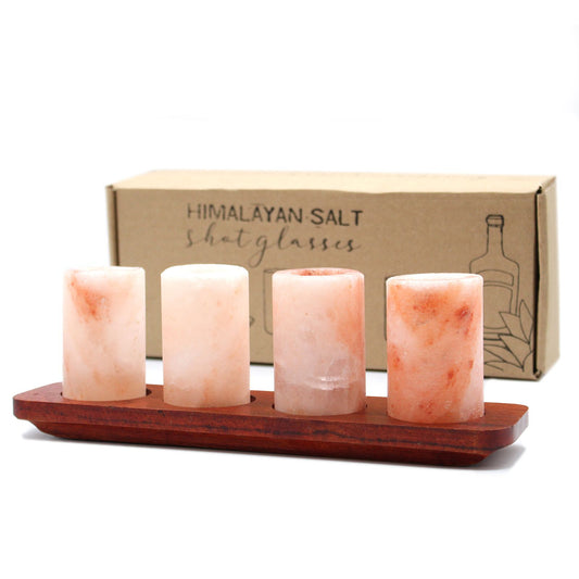 Four pink Himalayan salt shot glasses arranged on a rustic wooden serving stand with circular carved slots.