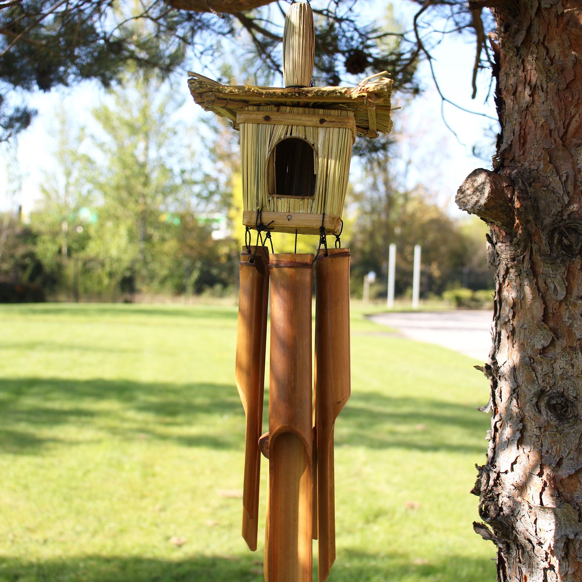 Square woven seagrass bird house with hanging bamboo chimes and a natural rope loop for hanging.