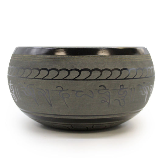 Handcrafted brass singing bowl with an engraved Buddha design and a wooden striker on a decorative cushion.