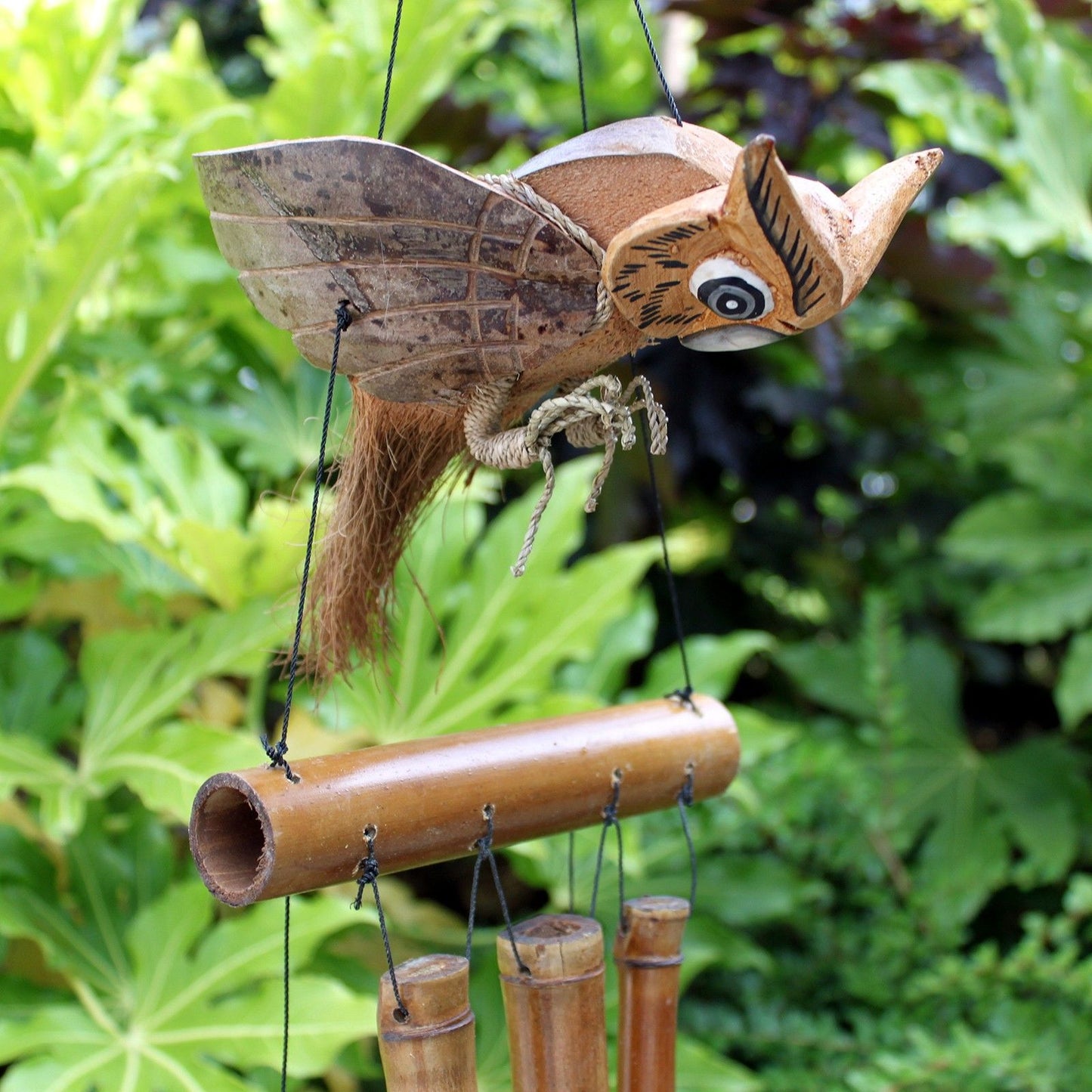 Handmade owl wind chime crafted from natural coconut and bamboo hanging outdoors.