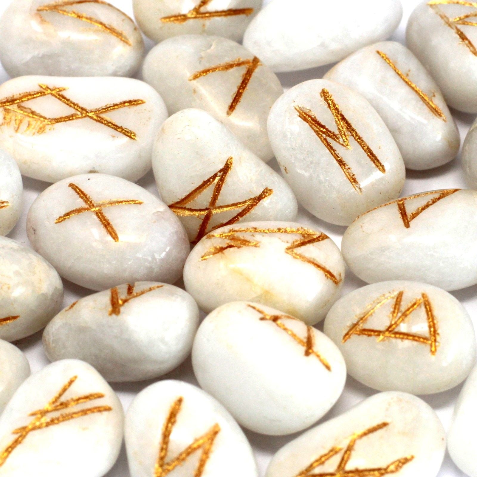 Polished white agate rune stones with engraved gold lettering spread out next to a small black drawstring pouch.