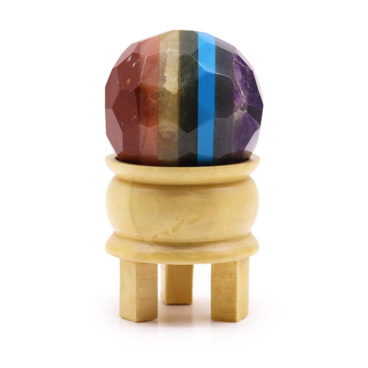 Multi-coloured faceted gemstone sphere representing the seven chakras resting on a light brown wooden stand.