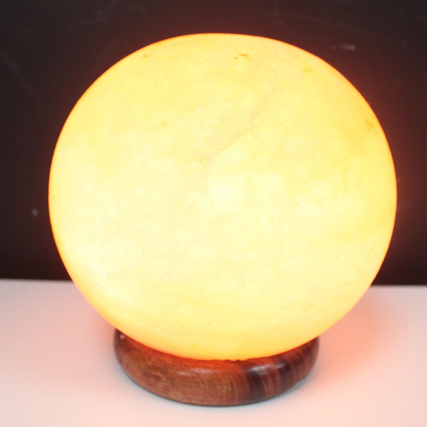 A glowing spherical Himalayan salt lamp resting on a sturdy round wooden base.