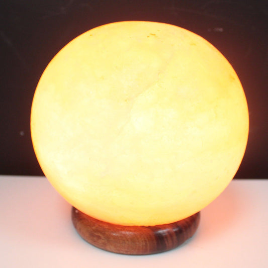 A glowing spherical Himalayan salt lamp resting on a sturdy round wooden base.