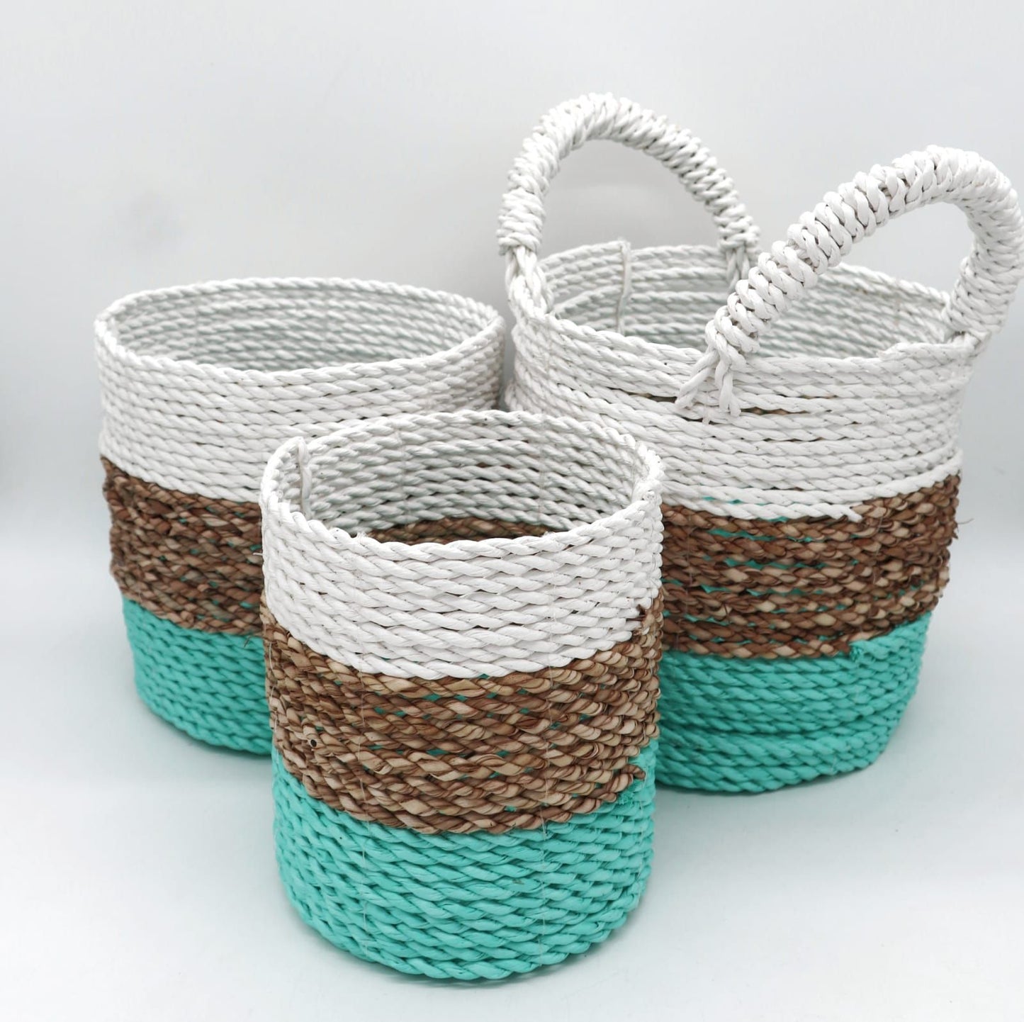 Three round handwoven seagrass baskets in green, natural, and white, nested together.