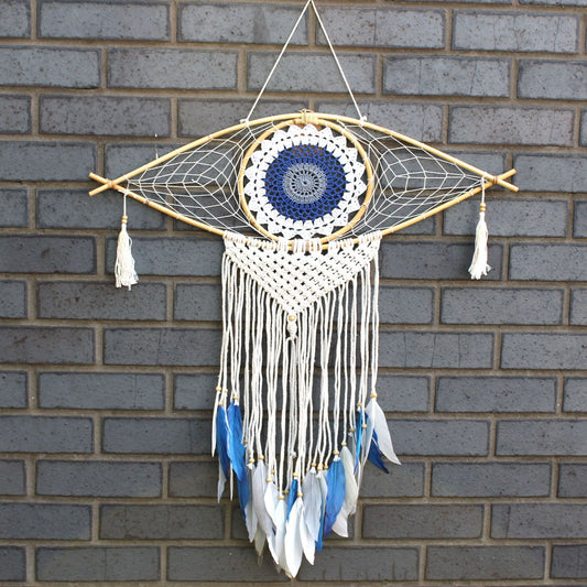 Large intricate macrame dream catcher with an evil eye design in white, blue, and grey cotton threads.