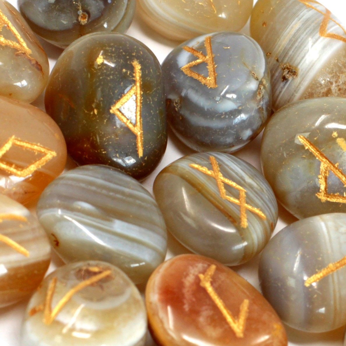 Hand-carved banded agate rune stones with silver engravings displayed alongside a small drawstring pouch.