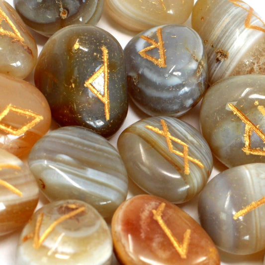 Hand-carved banded agate rune stones with silver engravings displayed alongside a small drawstring pouch.